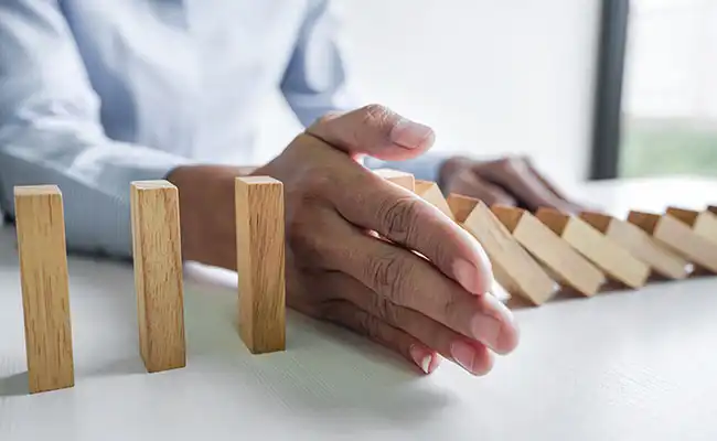 Mano deteniendo una cadena de fichas de dominó como representación de la gestión y prevención de riesgos empresariales que Elan Asesores puede hacer por sus clientes como asesor empresarial en Zaragoza